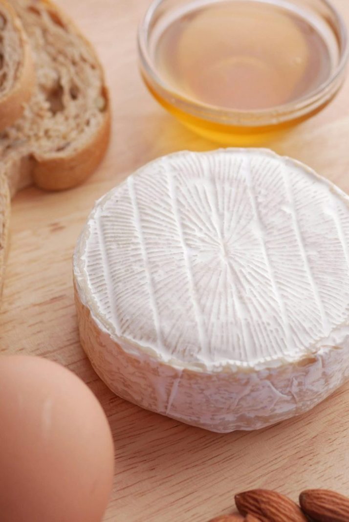 A delicious flat lay of camembert cheese, bread slices, honey, almonds, and a fresh egg for food inspiration.