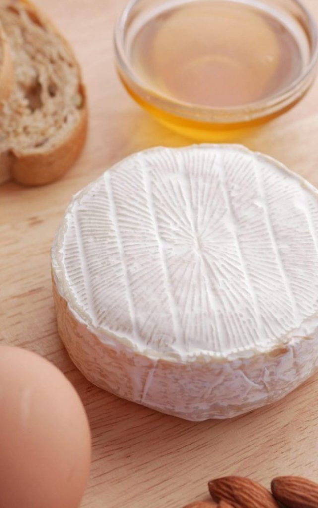 A delicious flat lay of camembert cheese, bread slices, honey, almonds, and a fresh egg for food inspiration.