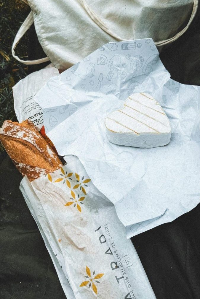 Flat lay of heart-shaped cheese, baguette, and tote bag, perfect picnic scene.