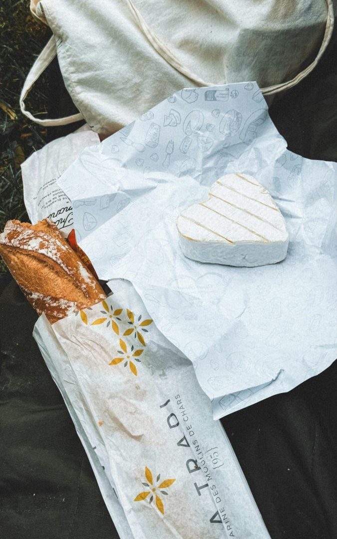 Flat lay of heart-shaped cheese, baguette, and tote bag, perfect picnic scene.