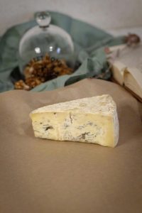 A slice of creamy Brie cheese on rustic paper, garnished with walnuts.