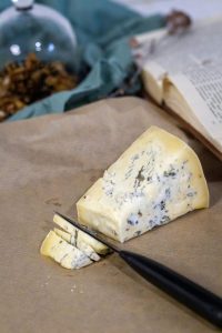 A slice of blue cheese with knife on rustic paper next to a book, perfect for culinary themes.