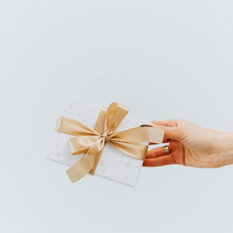 A hand holding an elegantly wrapped gift box with a gold ribbon on a white background.