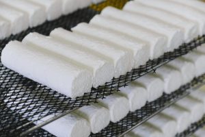 Fresh cheese rolls maturing on a wire rack in a cheese factory, showcasing food preparation.