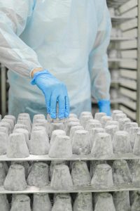 A worker in protective gear inspects matured cheese in an industrial setting, ensuring hygiene and safety standards.