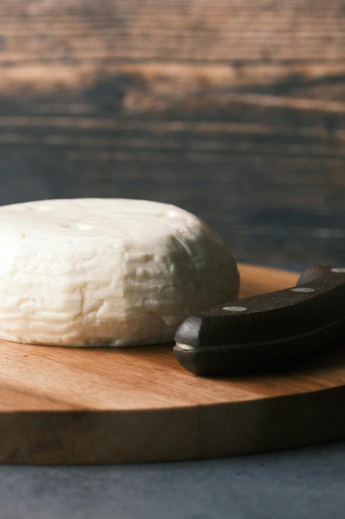 Round cheese on a rustic wooden board with a knife, depicting simplicity and gourmet appeal.