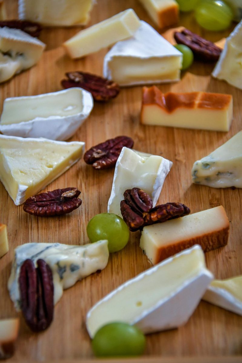 An assortment of gourmet cheeses and pecans on a wooden serving board.